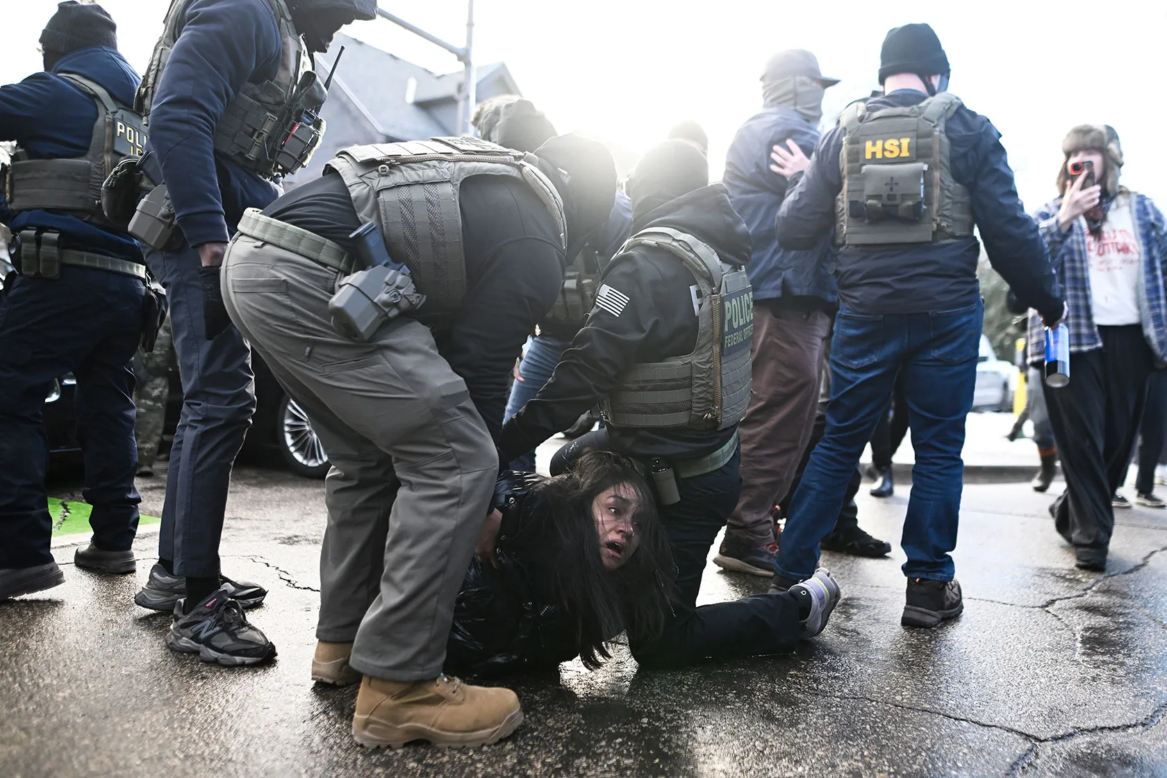Federal agents pinning a young woman to the pavement during an ICE arrest
