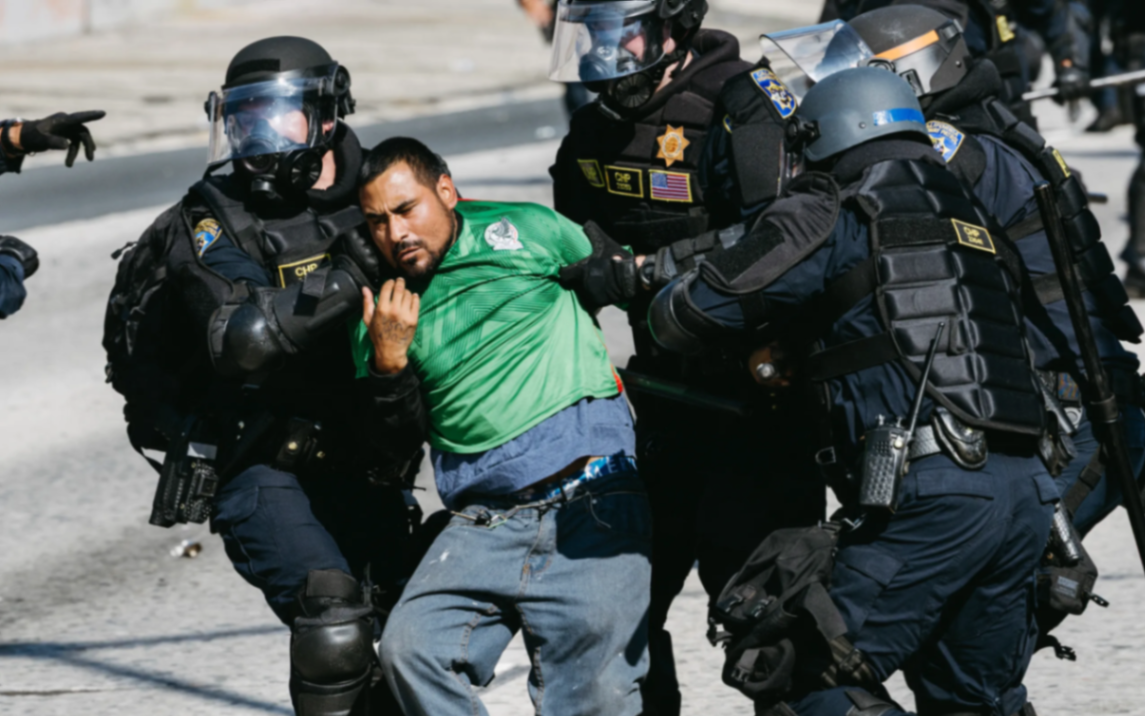 Riot police forcibly detaining a man at an immigration enforcement operation